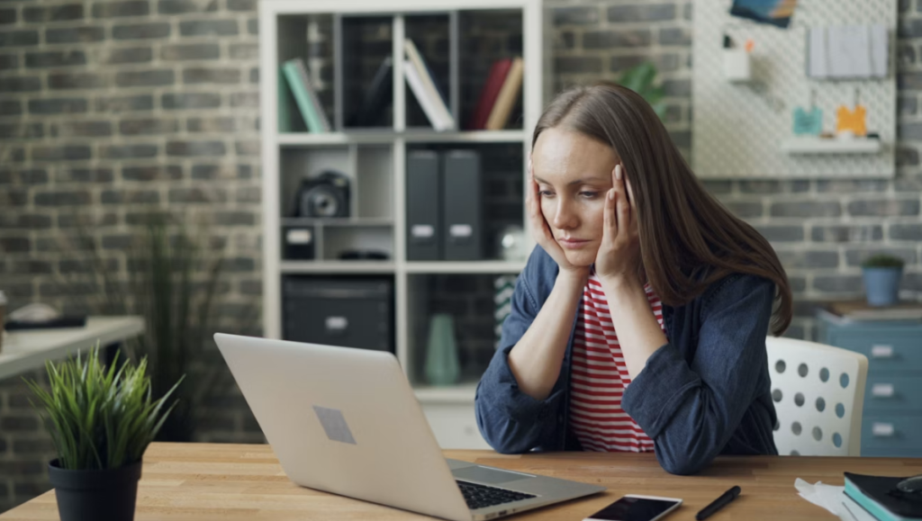 Woman sat at a desk looking frustrated at her laptop