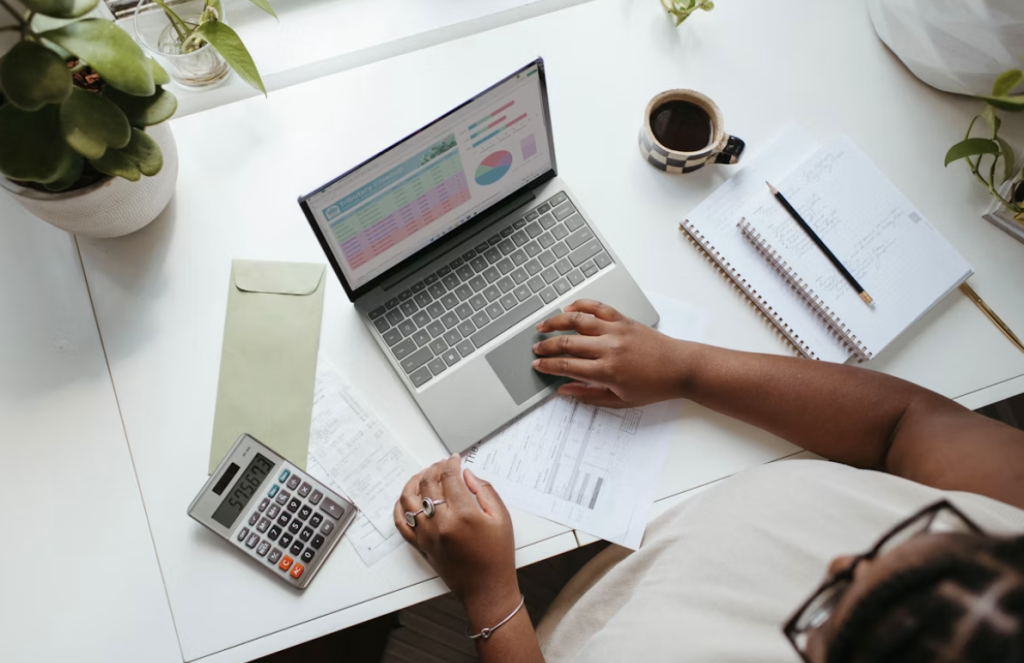 Woman sat on a laptop at a desk with a mug of coffee working on data and budgets